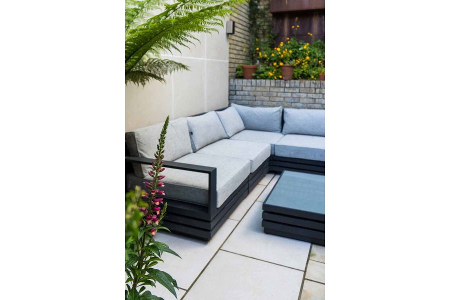 Outdoor furniture sits on Light Grey Porcelain paving slabs around glass table in small garden setting with palm trees.