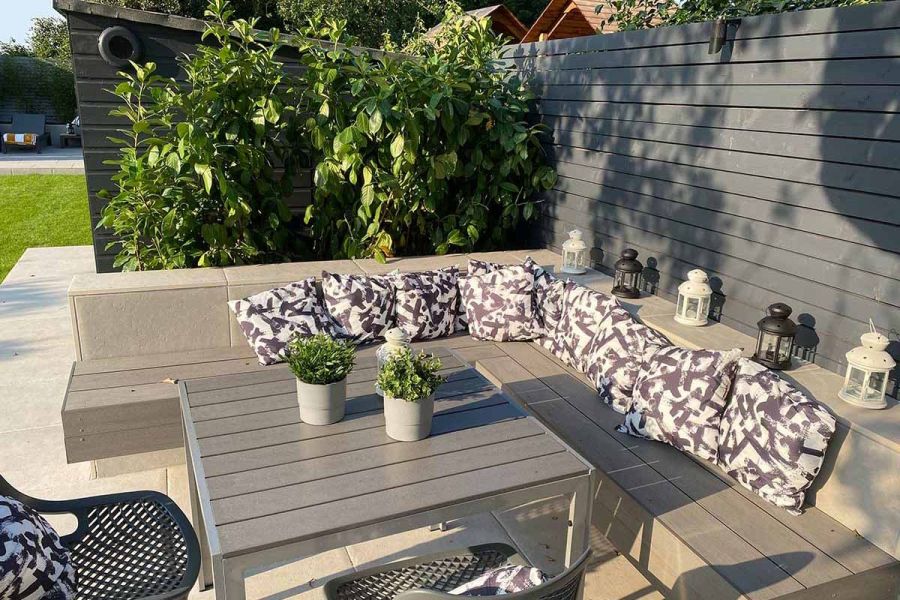 Cantilevered bench and matching table with deck fascia boards in Pebble Grey Brushed composite, by the garden fence with potted plants.