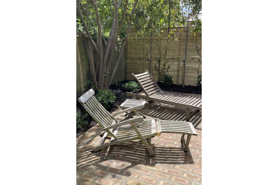 Two sunloungers casting shadows on london mixture clay paver patio with fence and tree in the background.