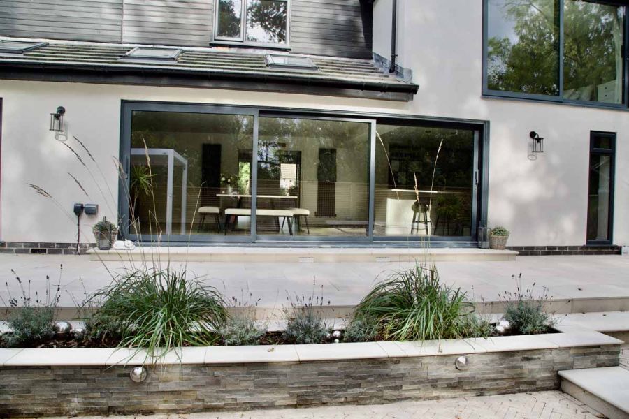 Huge french doors on white house lead onto ash beige porcelain patio using matching steps and copings.