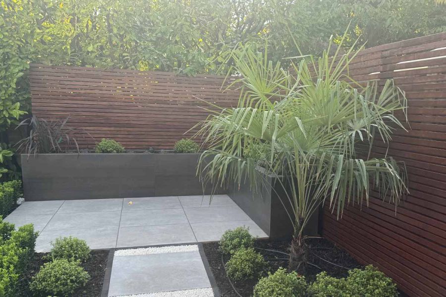 Batten clad fence with large trees surrounding shows patio with built in planters using with metal dark premium designclad.