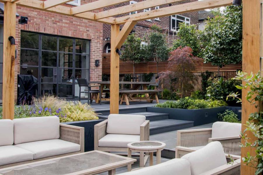 Wooden pergola sat over beige outdoor furniture with black basalt composite decking used on steps and elevated patio.