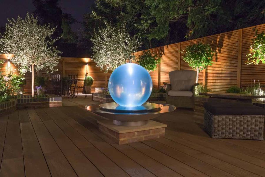 Olive trees light up in the dark with sphere water feature creating a glow on coppered oak millboard decking.