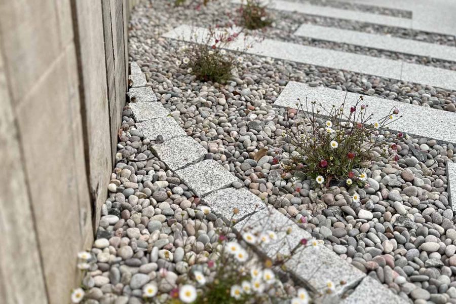 Close up of Natural Silver Grey Granite Setts in circular design surrounded by light pebbles and matching paving slabs.