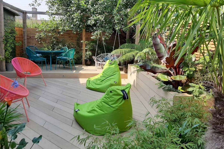 Amber Classic DesignBoard decking and fascia boards, with two green beanbags and two orange chairs, a swing seat, and slatted fencing.