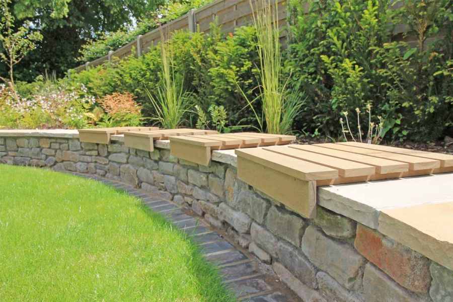 Close up of curved, built-in bench using sandstone and warm teak composite battens with flowerbeds behind, in unique design