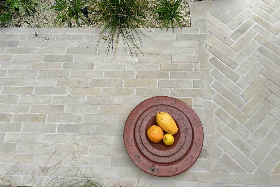 Ornamental bowl of fruit sits on beige sandstone patio bricks shown laid in two styles in garden design.