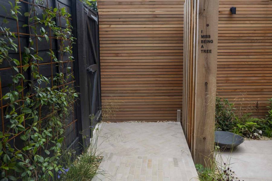 Slatted fence panels with feature panels noting 'I miss being a tree' with beige sandstone patio brick path.