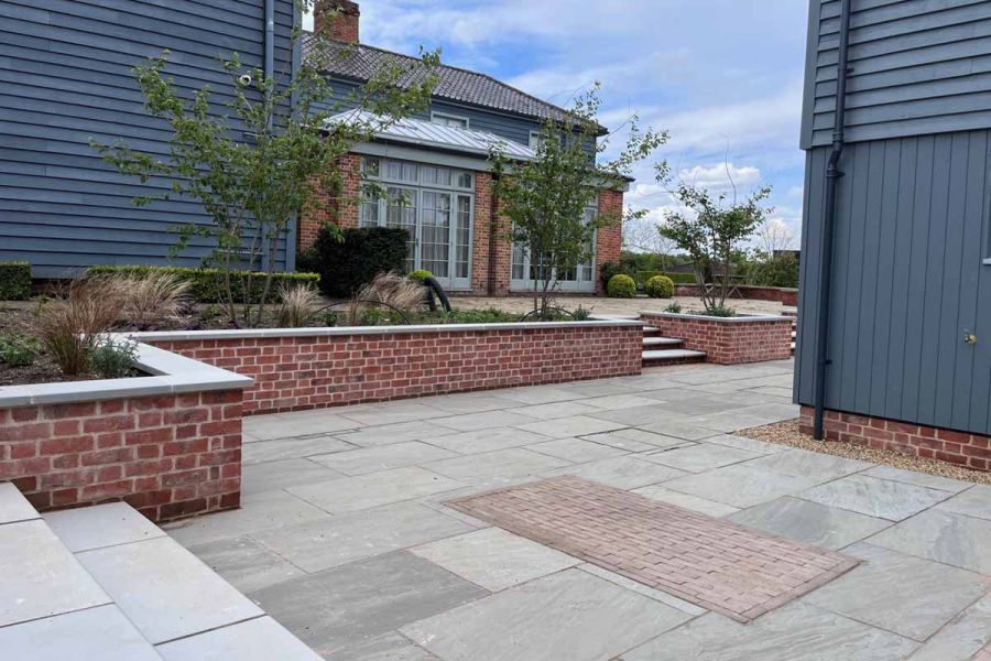 Brick flowerbeds clad with grey sawn sandstone sit on kandla grey indian sandstone paving with clays laid in rectangle pattern in between.