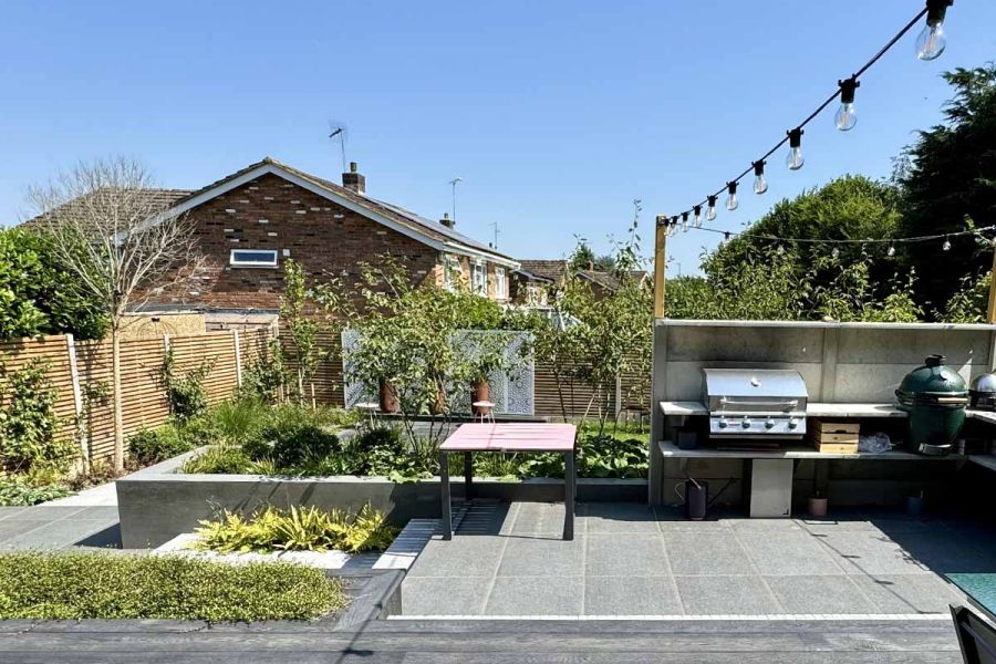 Raised patio using black basalt porcelain hosts outdoor cooking area with steps leading down to lower part of the paved area.