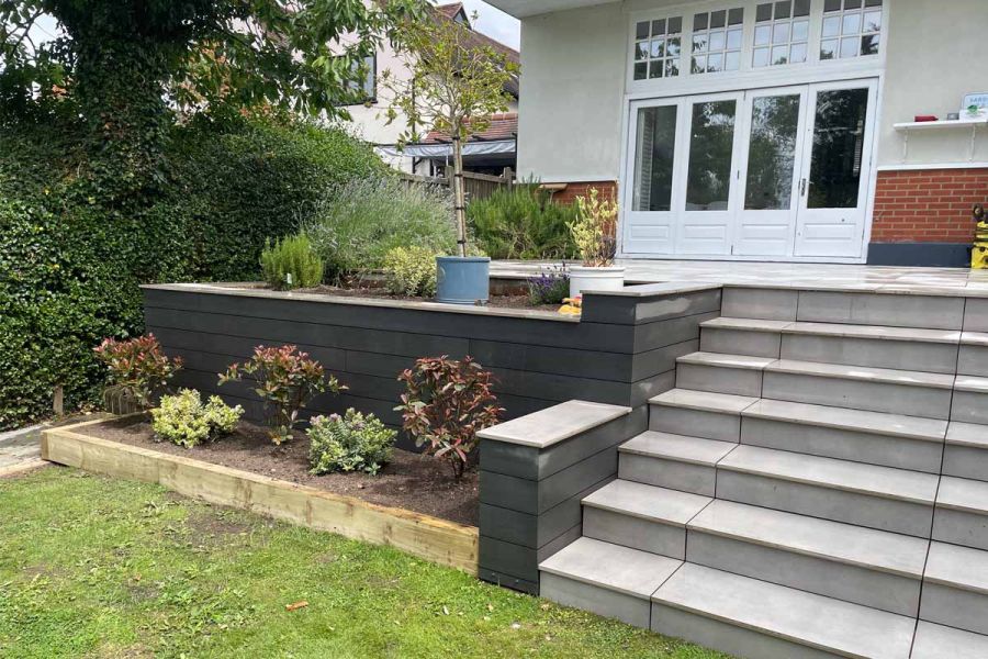 Porcelain steps lead up to patio with raised flowerbeds clad with Pebble Grey Brushed Composite Decking.