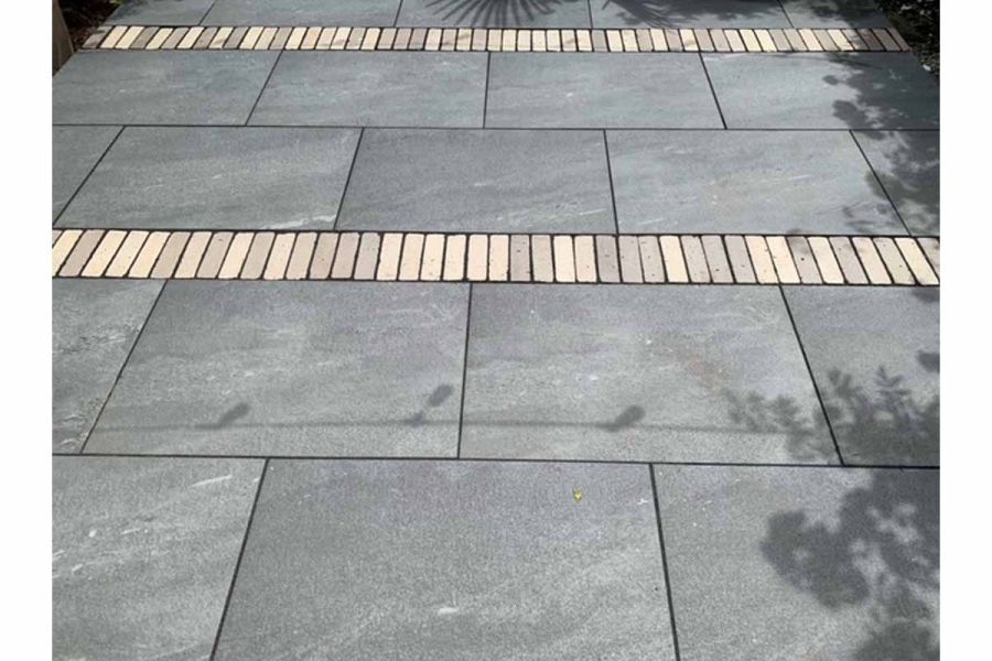 Close up view of Platinum Grey Porcelain Paving with 2 rows of clay pavers running through the patio, washing-line and trees cast shadows.