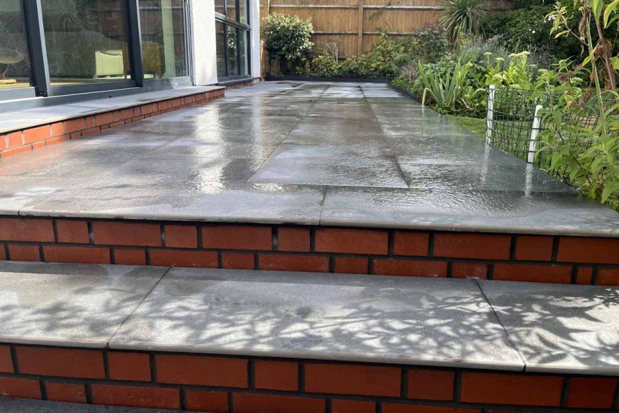 A tiered patio showcases Platinum Grey paving with 20mm bullnose steps, set against a white house with steps rendered in red brick.