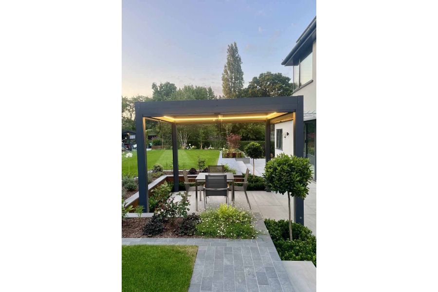 Dusk view shows proteus pergola with led lights above porcelain patio with platinum grey porcelain setts as path leading towards.