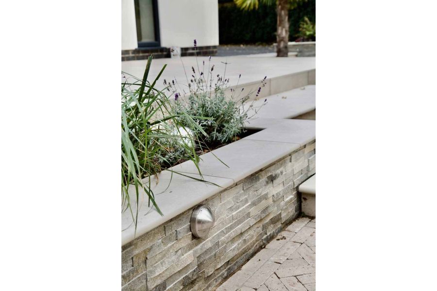 Close up of raised flowerbed clad with stone walling and capped with ash beige porcelain 20mm bullnose coping stones.