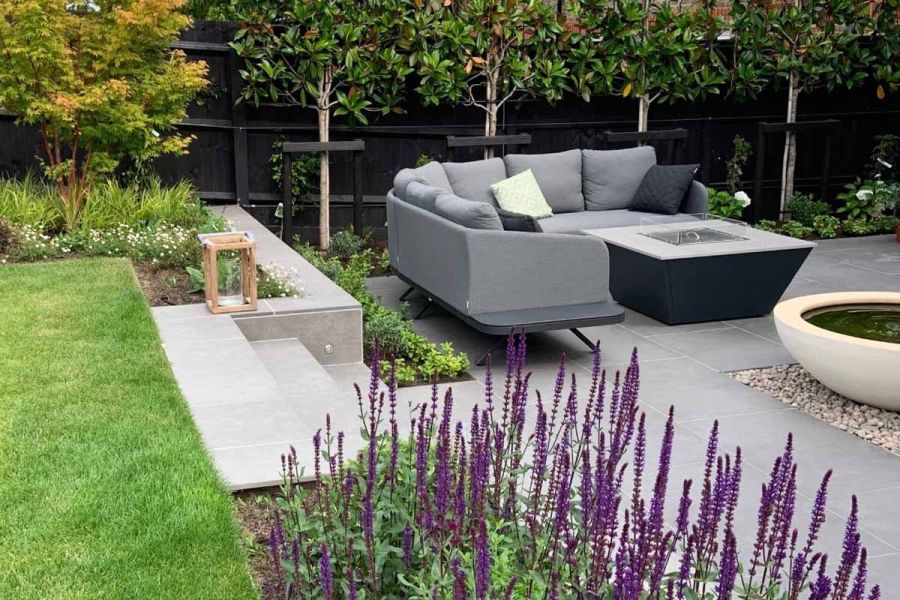 Steel Grey porcelain garden steps lead down to patio area with garden furniture, fire-pit and water feature.