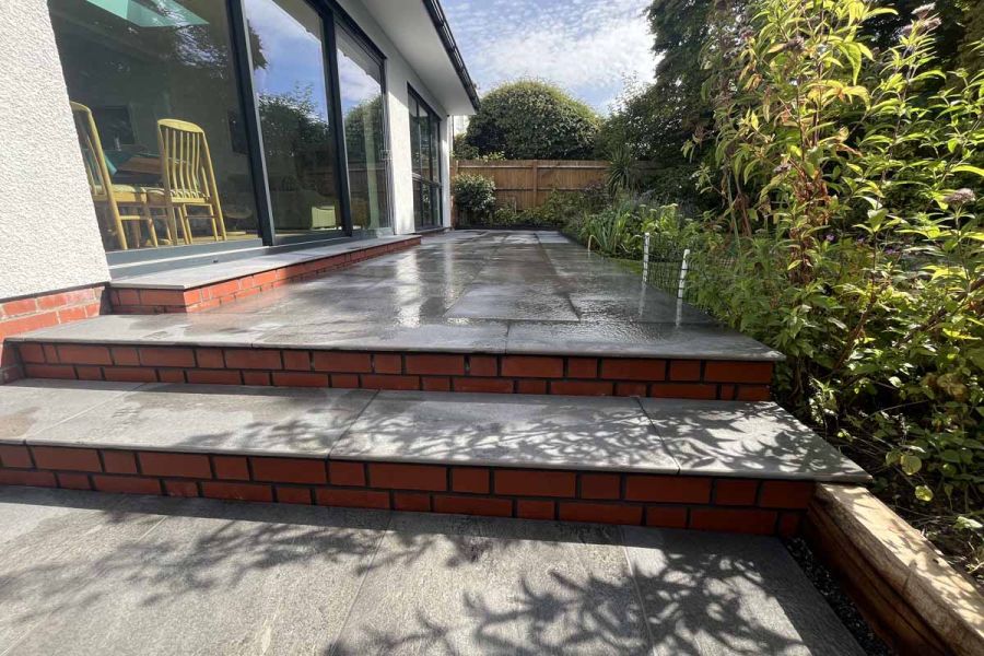 Multi level patio uses platinum grey paving and 20mm bullnose steps against white house with red brick rendered steps.