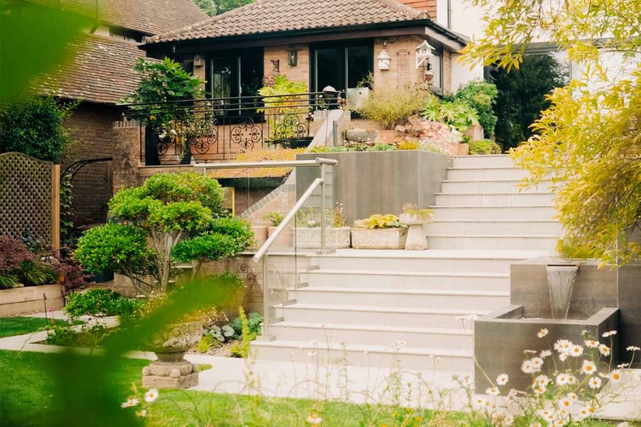 Blurred view through foliage show impressive outdoor staircase using kandla grey porcelain 20mm bullnose steps and matching paving.