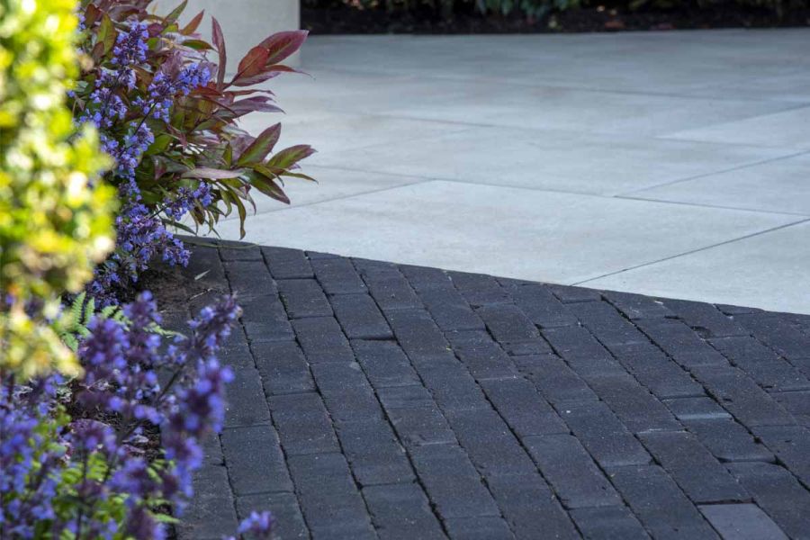 Close view through foliage of charcoal grey clay pavers and cream porcelain at RHS Tatton Park Flower Show 2024.