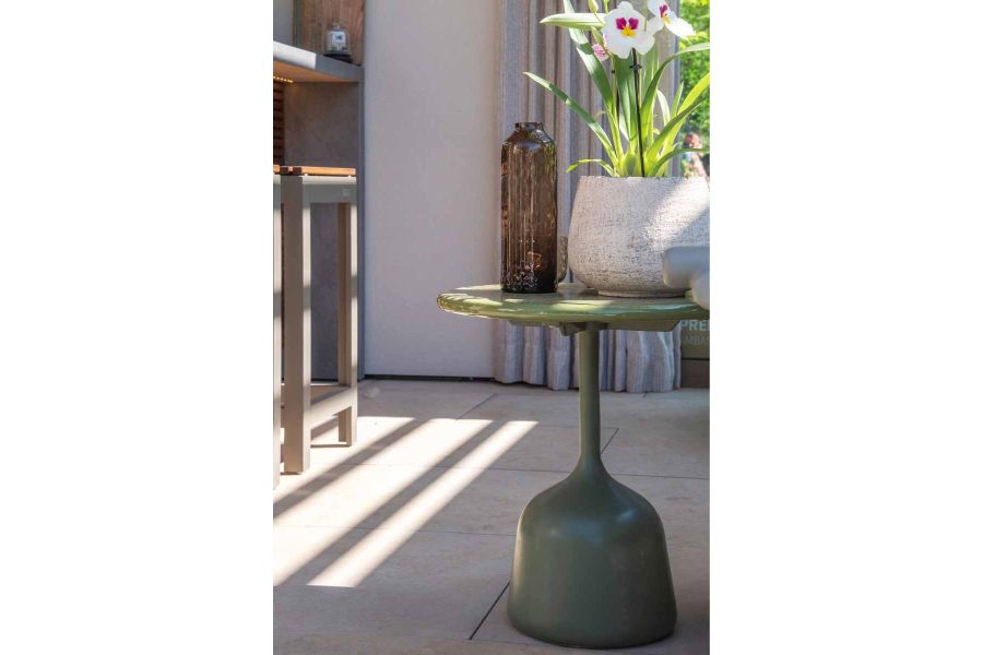 Arty shot of table that looks like an upside down wine glass, with vase and plant pot on top, sits on Jura Beige porcelain paving at RHS Chelsea.