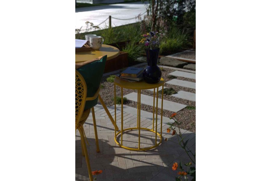 Yellow metal furniture sits on egyptian beige limestone pavers at RHS Tatton Park Chelsea Flower Show.