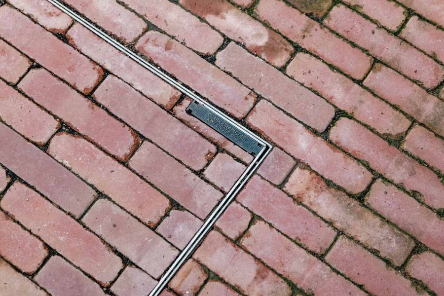 Section of roma brick pavers laid over manhole, clays inset in the drainage cover in traditional pattern.