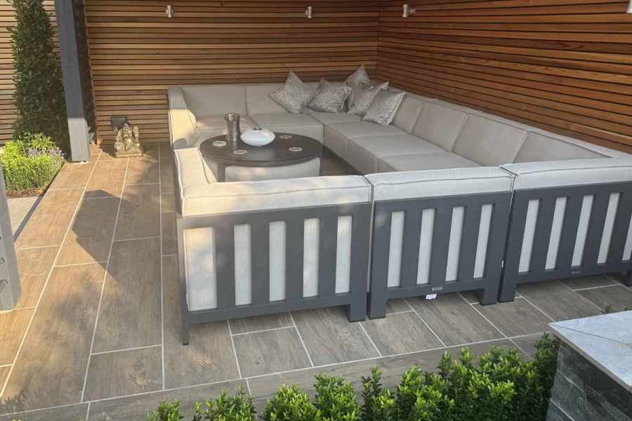 Large outdoor lounging set with cushions sits under pergola on wood-inspired rovere porcelain paving.