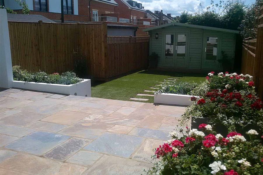 sunny views from front of back garden show a rustic slate paving patio with steps leading down to lawn area.