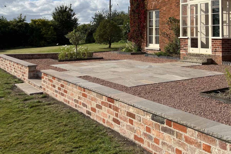 Red brick wall capped with autumn brown indian rock-faced coping stones create barrier between lawn and patio.