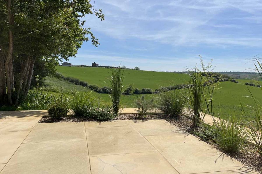 Harvest sawn sandstone paving forms the patio, with flowerbed insets and impressive countryside views in the background.