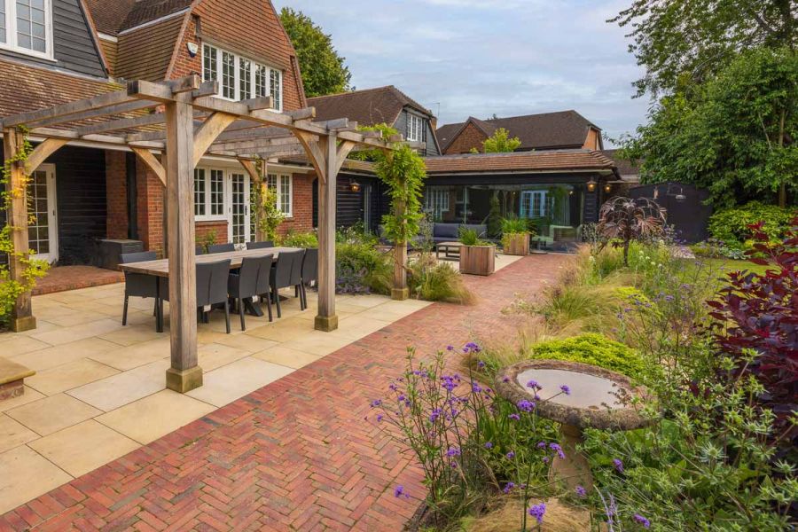 Wooden pergola sits on sandstone patio with seville clay paver path making a break between patio and lawn.