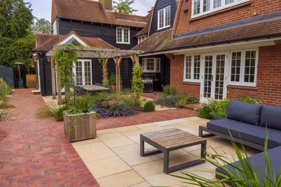 Seville Clay Pavers with sandstone patios inset, one host to lounge furniture and one to a dining table under wooden pergola.