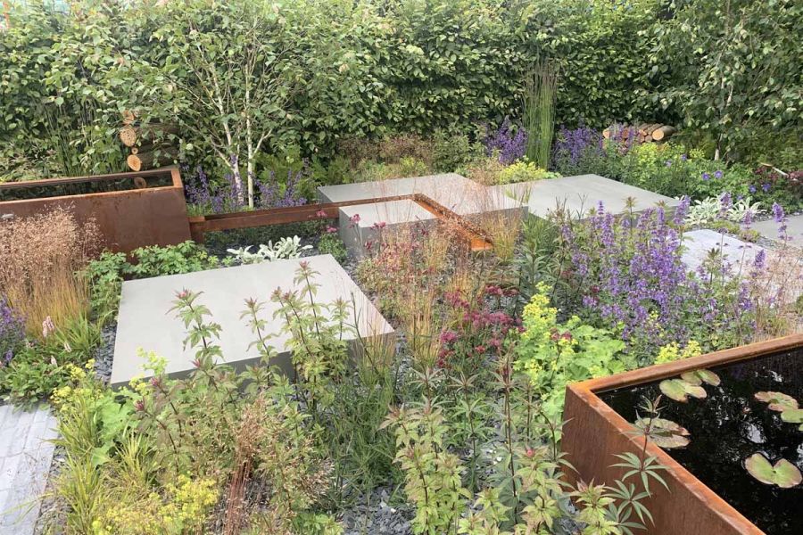 Sidewalk 1200x1200 porcelain paving, surrounded by green and purple plants and corten water features at BBC Gardeners' World Live 2024.