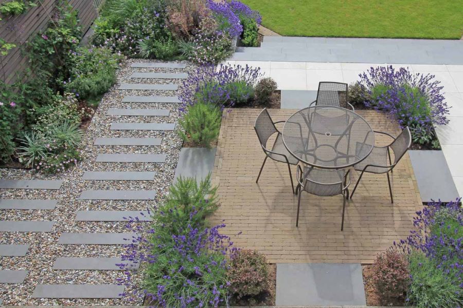 Birds eye view of garden using steel grey porcelain planks set between pebbles, paving and clay pavers hosting patio furniture.