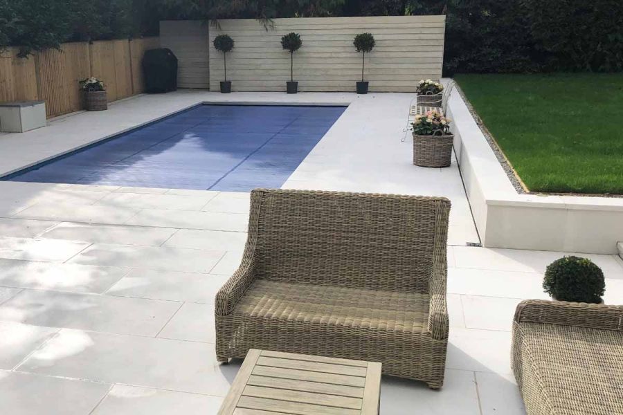 Swimming pool and lounge furniture on porcelain patio with raised flowerbeds capped with comblanchien 40mm downstand copings stones.