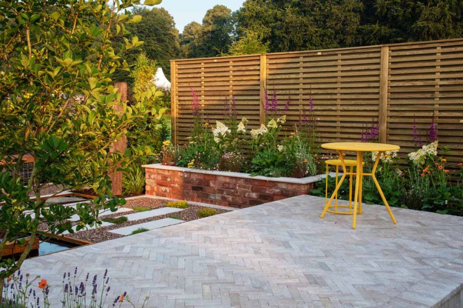 Egyptian Beige stone pavers forming a sleek patio through a show garden, showcasing their soft, sawn and tumbled finish.