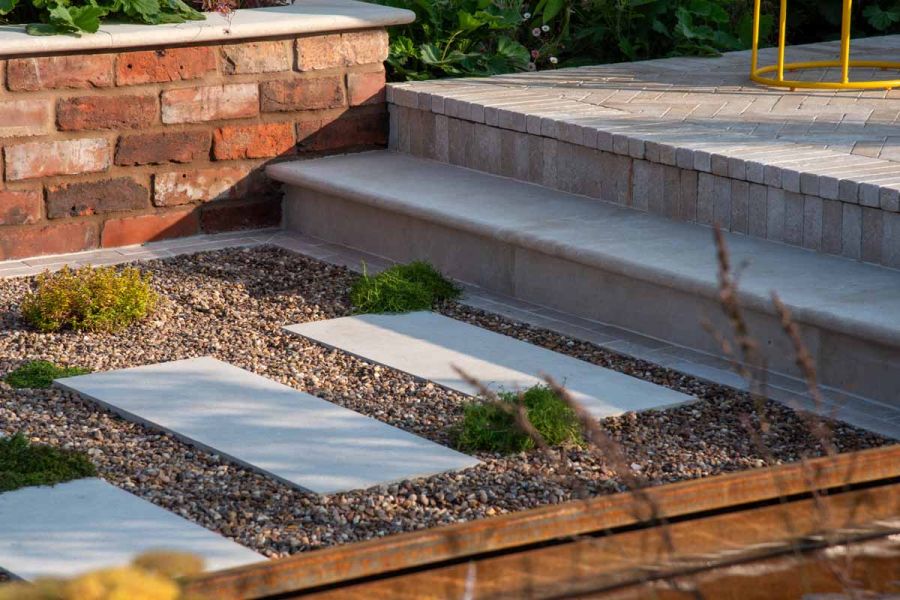 One egyptian beige limestone bullnose step leads down to stepping stone path surrounded by pebbles at RHS Tatton Park Flower Show 2024.