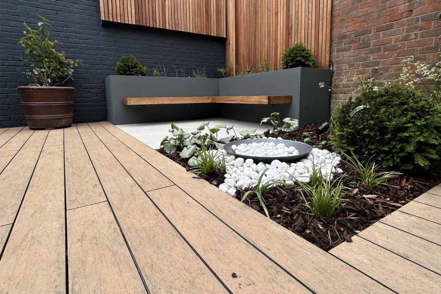 Porcelain paving flanks the warm teak brushed composite decking, featuring a floating bench and surrounding plants.