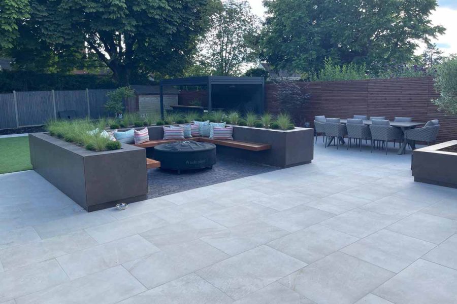 Large entertaining area with raised planter area sectioned off for seating, dining table and pergola in the distance.