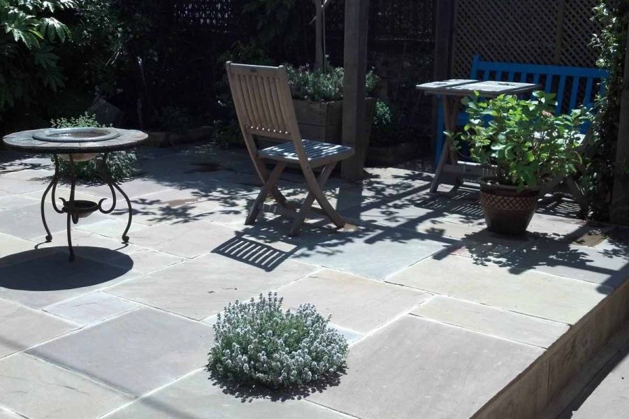 Sunny patio with chairs and fire pit casting deep shadows onto Tumbled Raj Green project pack paving. Design by Coles and Jackson.