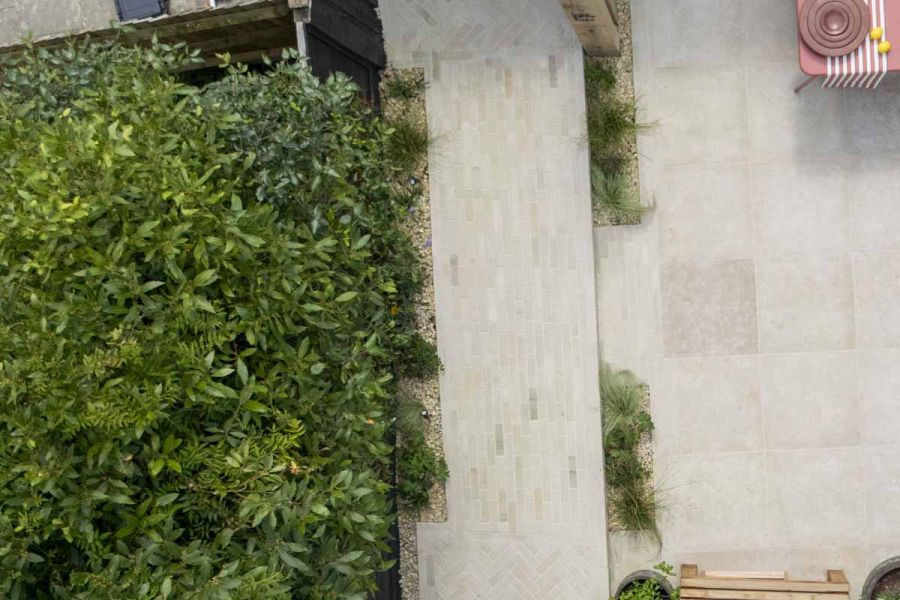 Aerial view of beige sandstone pavesr pathway next to limestone patio with bistro set and large green hedges.