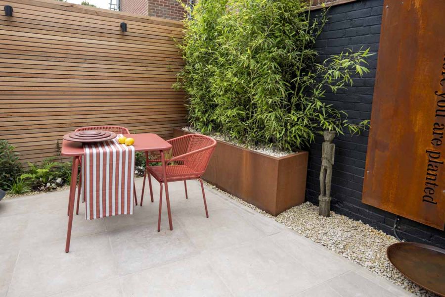 Corten steel panel seen on dark wall as feature, red bistro set sits on egyptian beige limestone patio.