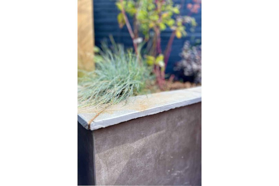 Close up view of Vulcano Ceniza Luxury DesignClad used on built in flowerbeds, planting seen out of focus in the background.