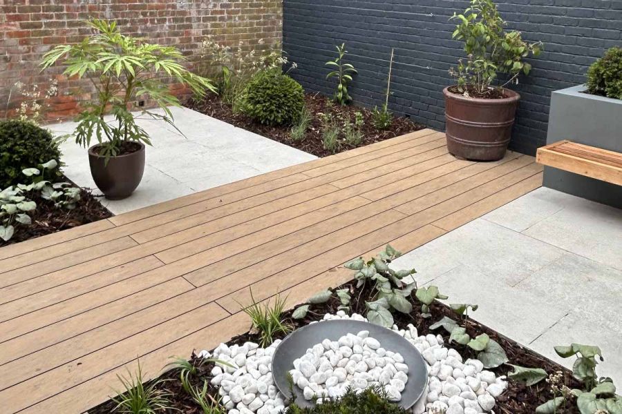 Porcelain paving either side of warm teak brushed composite decking with a floating bench and plating surrounding.