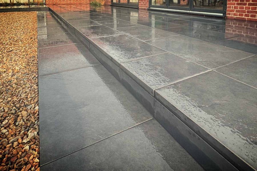 Close up side view of corner of small florence dark patio shown in the wet, with one garden step up showing downstand edges.