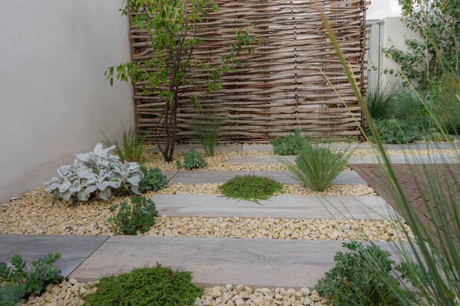 Staggered planks of cinder porcelain paving in stepping stone fashion has plants and pebbles between each tile.