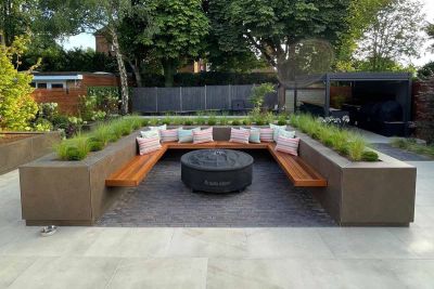 Patio with raised flowerbeds used as walls to contain floating bench and firepit, sitting on lugano clay pavers. Pergola in distance.***Trendy Landscapes
