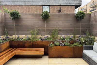 Chestnut Composite battens seen in the distance in front of floating bench, tall trees and stacked corten steel planters.***Chestnut Gardens
