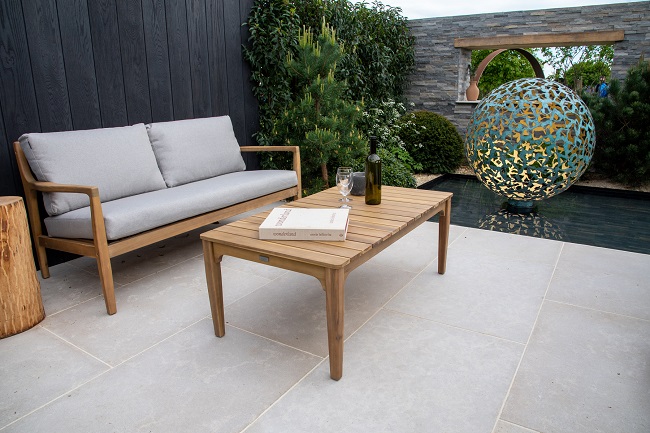 Wood-framed furniture on Egyptian Beige Limestone patio with dark fence, stone-clad wall at RHS Malvern 2022