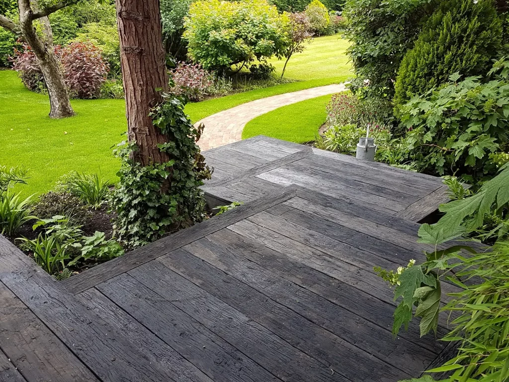 Platform steps of Embered Millboard descend between tree and planted bed to path curving through lawn.